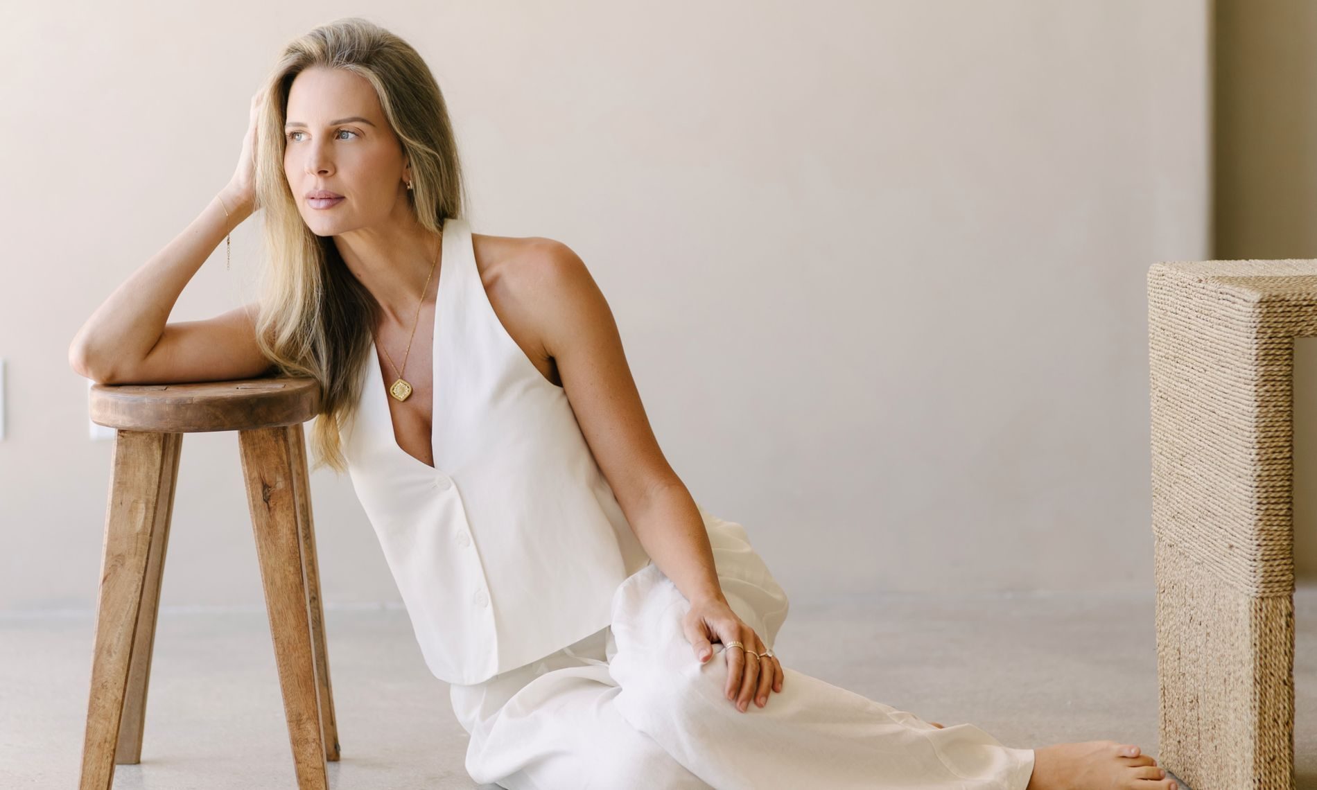 Elle Wilk seated on the floor beside a wooden stool, looking out
