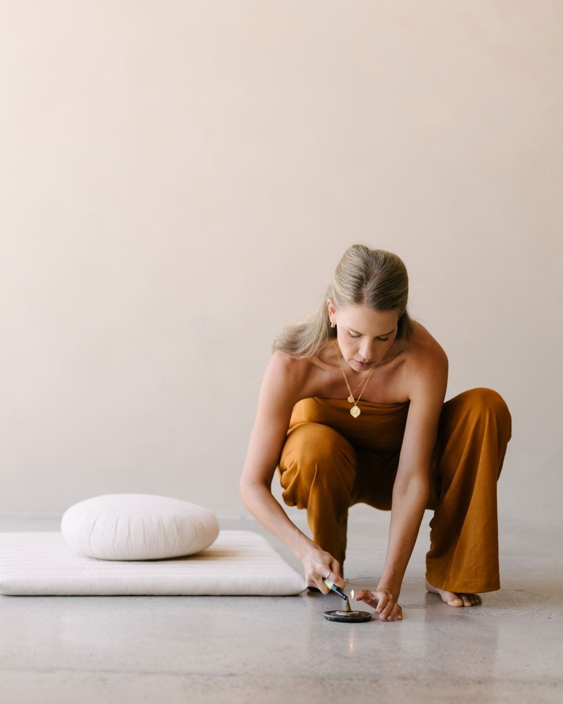 Elle kneeling on the floor, lighting incense beside a meditation cushion