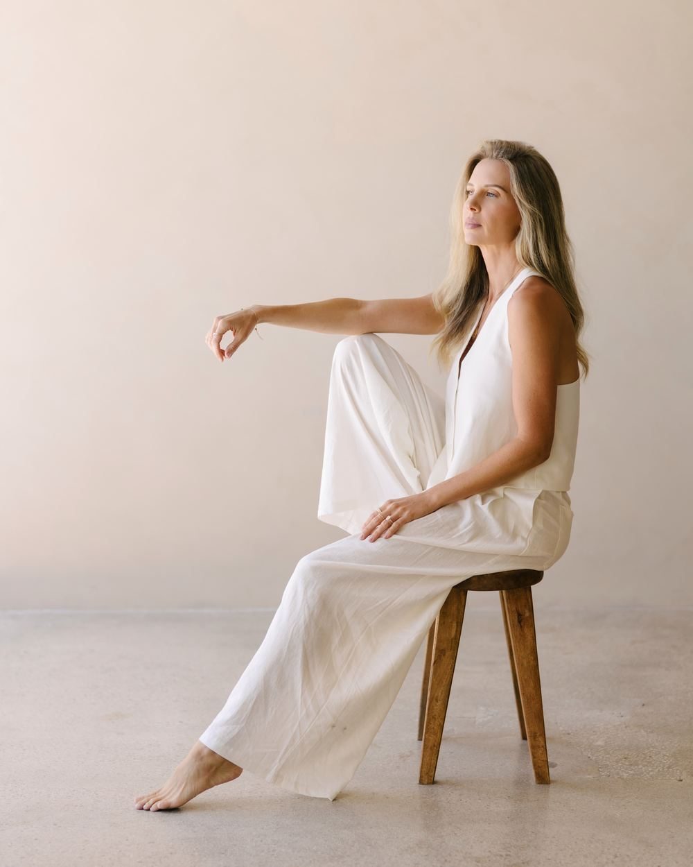 Elle seated on a wooden stool in white, looking out