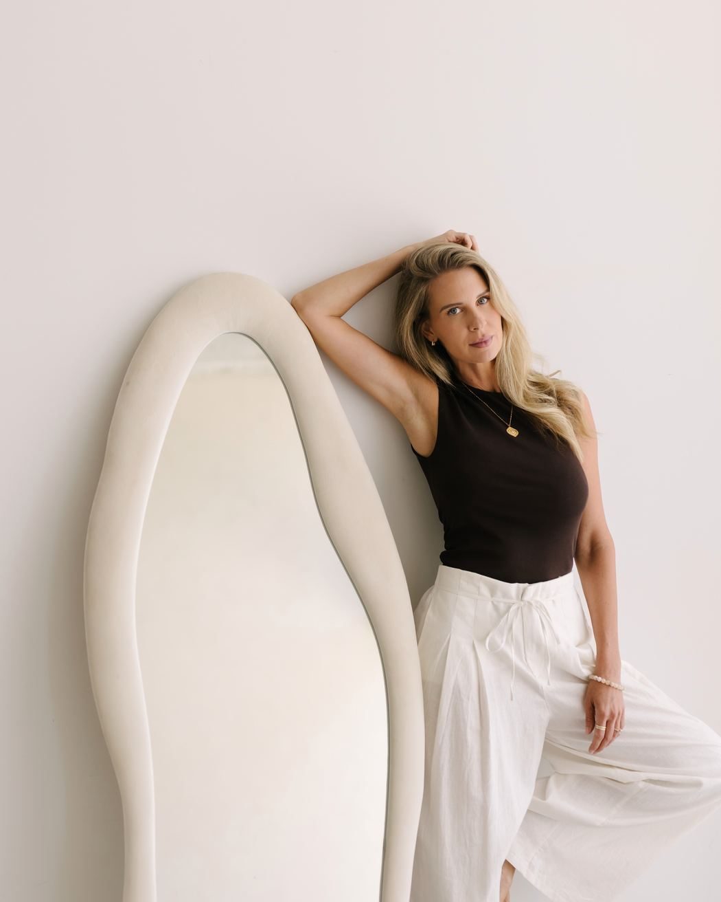 Elle leaning against a tall sculptural mirror